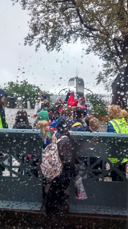 The Greenwich Meridian (marked by a stainless steel line and globe) viewed from behind Airy's transit telescope. School children line up along the line, which separates the west of the world on the left of the picture from the east of the world, on the right.  